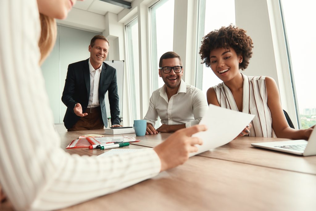 Great results! Group of young business people looking at documents and smiling while sitting at the office table. Brainstorming