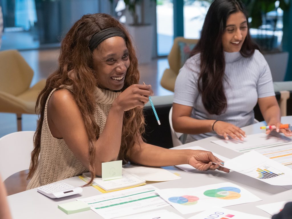 Two people engaged in a meeting with colorful paper and graphs on the table. one woman is laughing joyously.