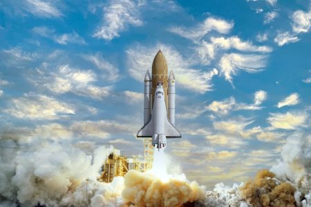 A space shuttle launches amid billowing clouds of smoke, ascending against a backdrop of a bright blue sky scattered with fluffy white clouds.